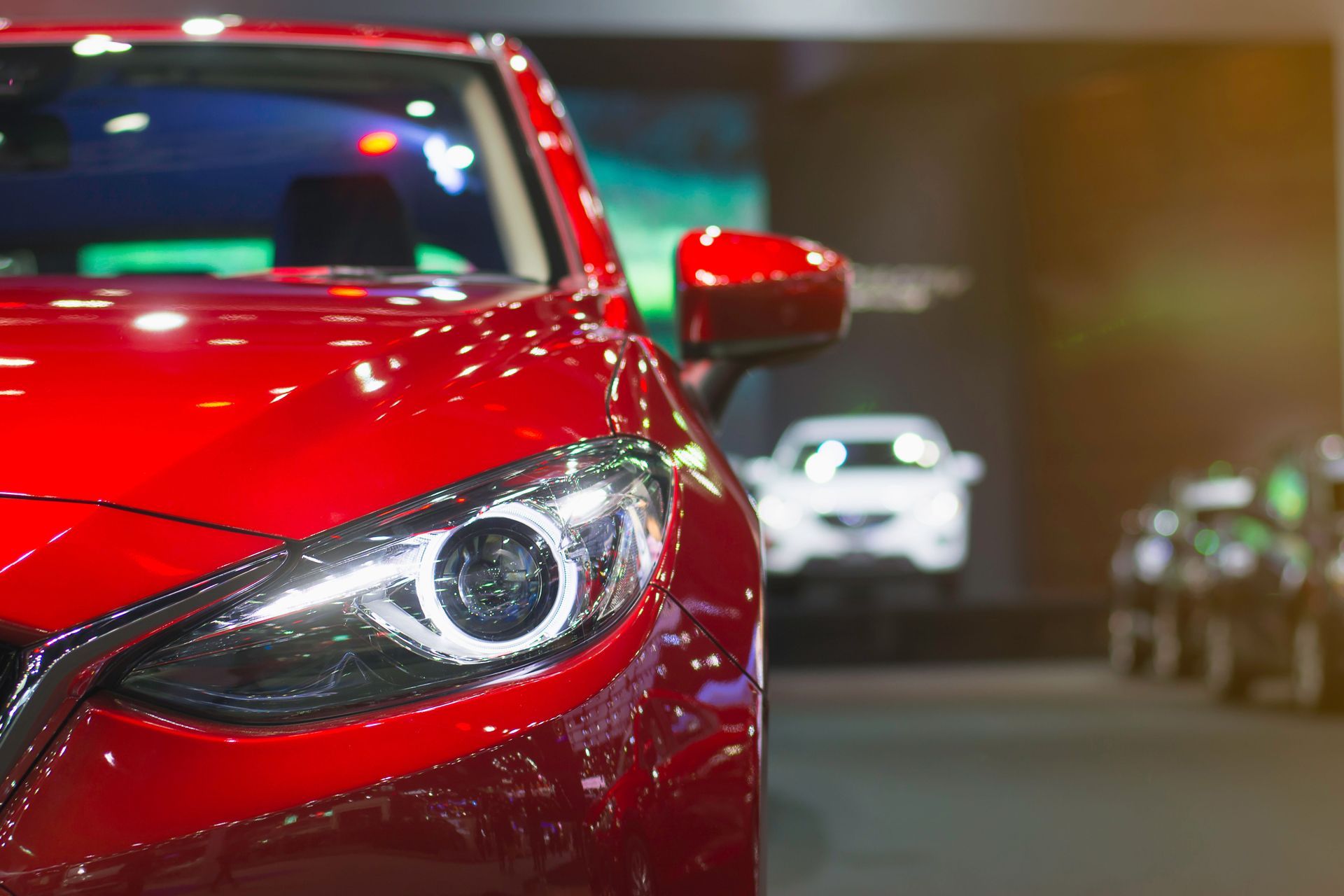 Red car on display at an auto show, with other cars in the background.