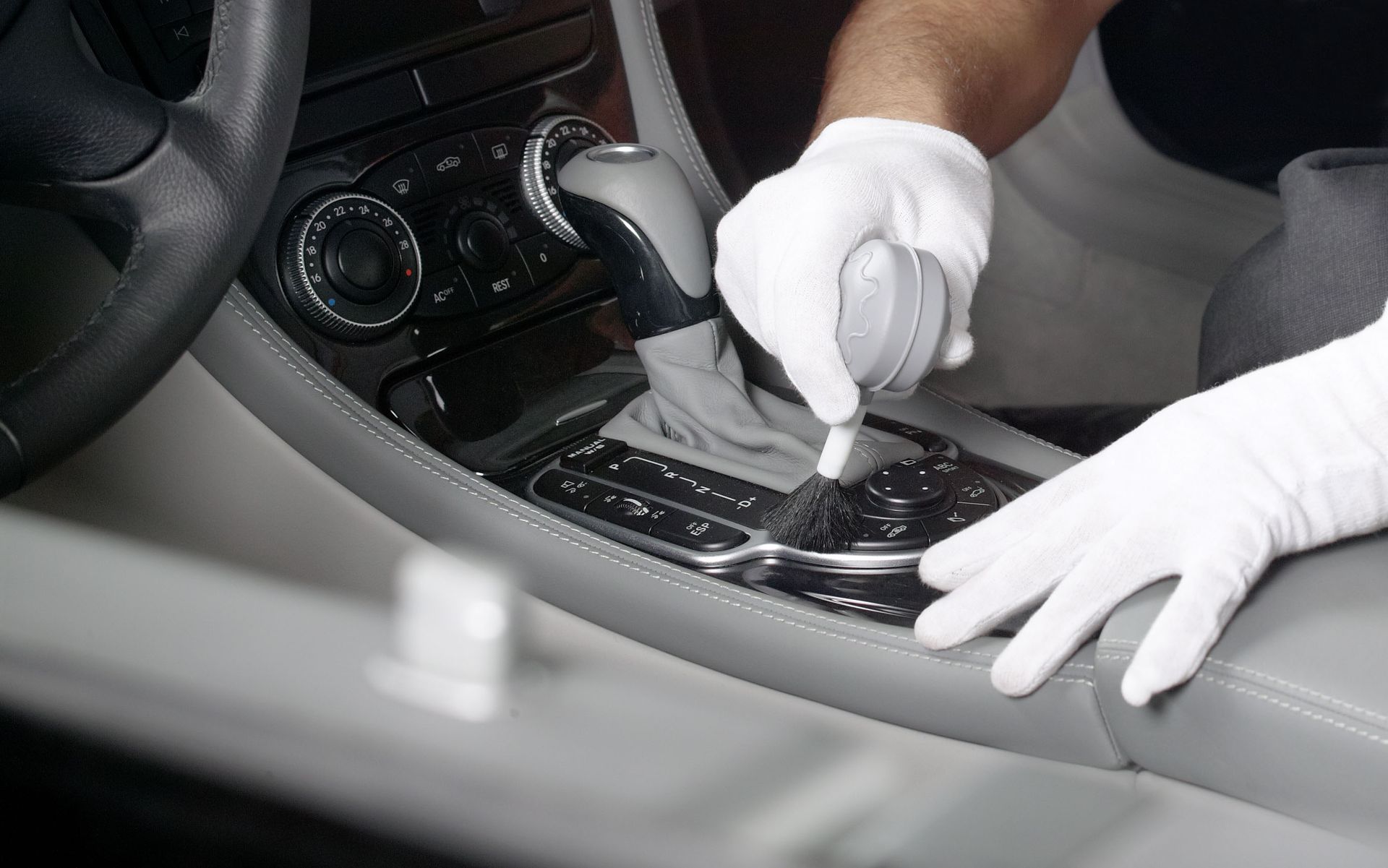 Person wearing white gloves cleaning a car's interior with a tool, including the gear shift area.