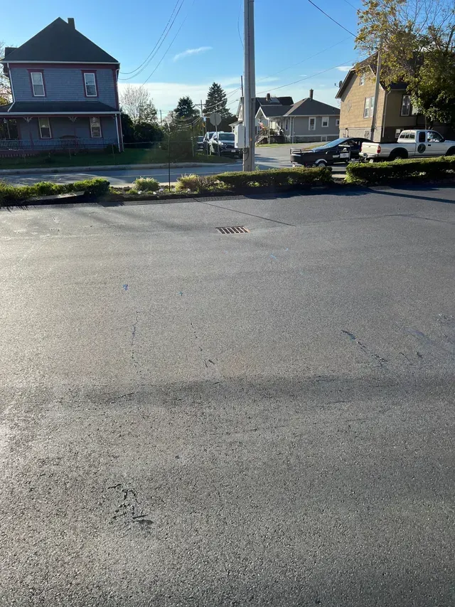 Quiet suburban street with parked cars, houses, and bright blue sky in the background.