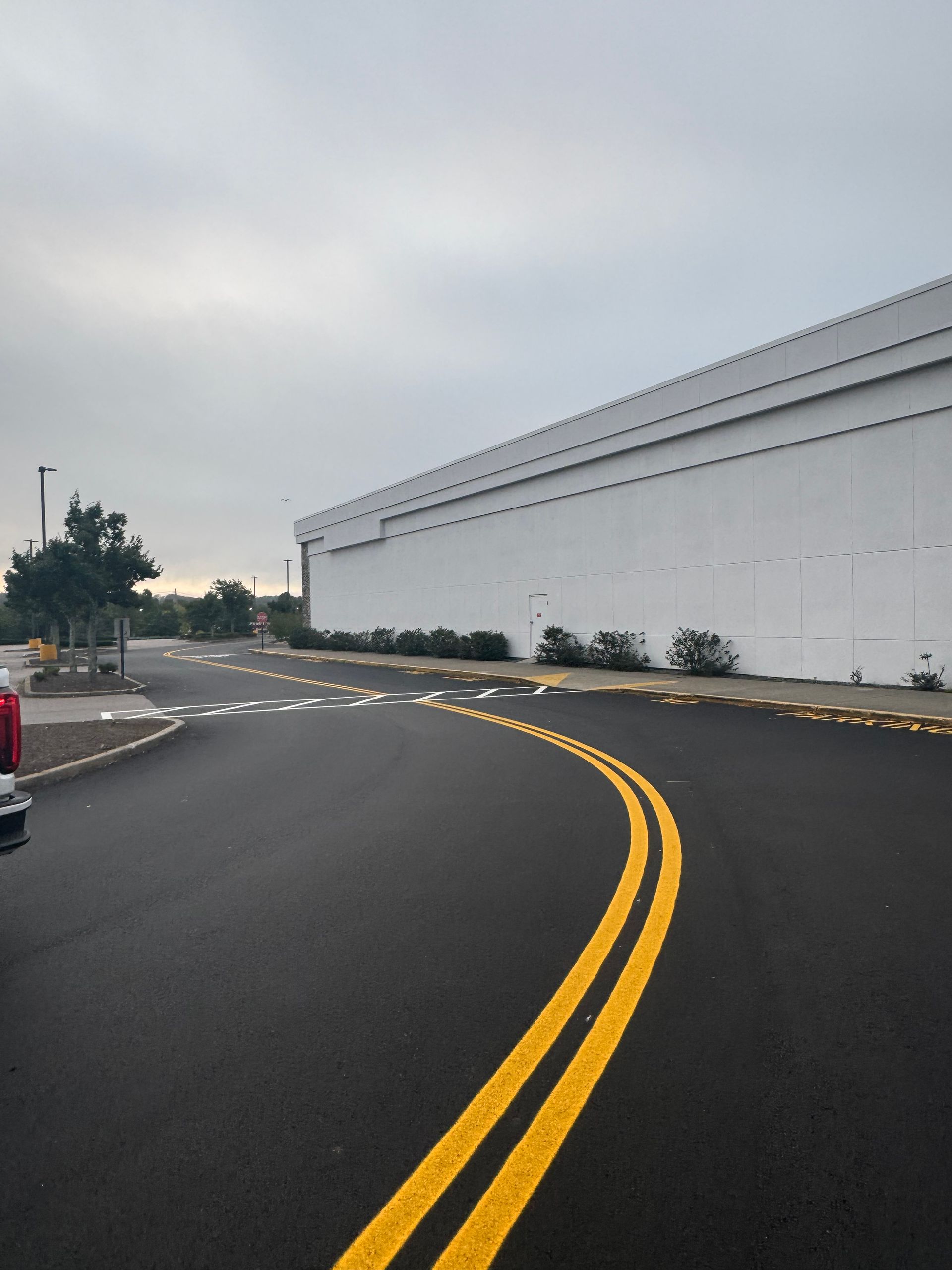 Curving wet road beside a long white building under a gray overcast sky