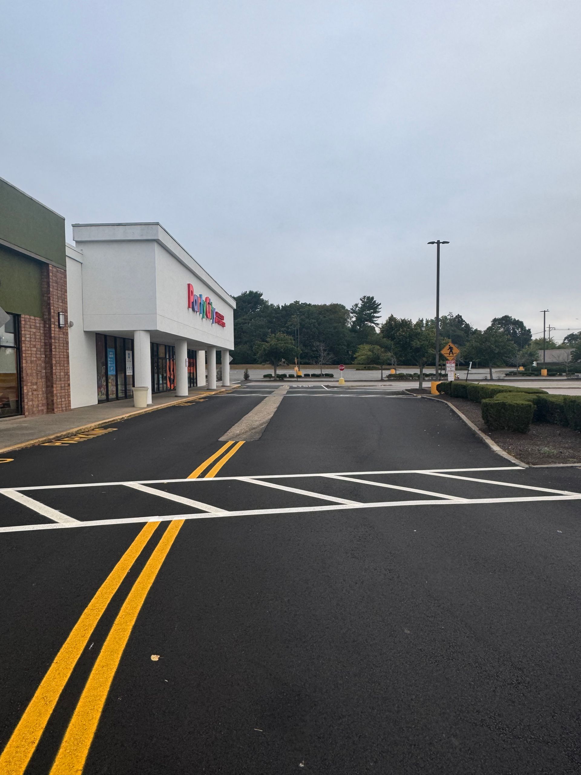 Empty parking lot beside a white storefront on a cloudy day, with yellow road lines and a crosswalk