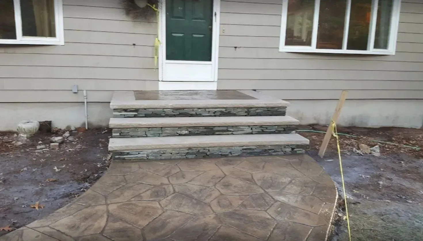 A tan house exterior with three stone steps leading to a green front door and a decorative stone-patterned concrete path.