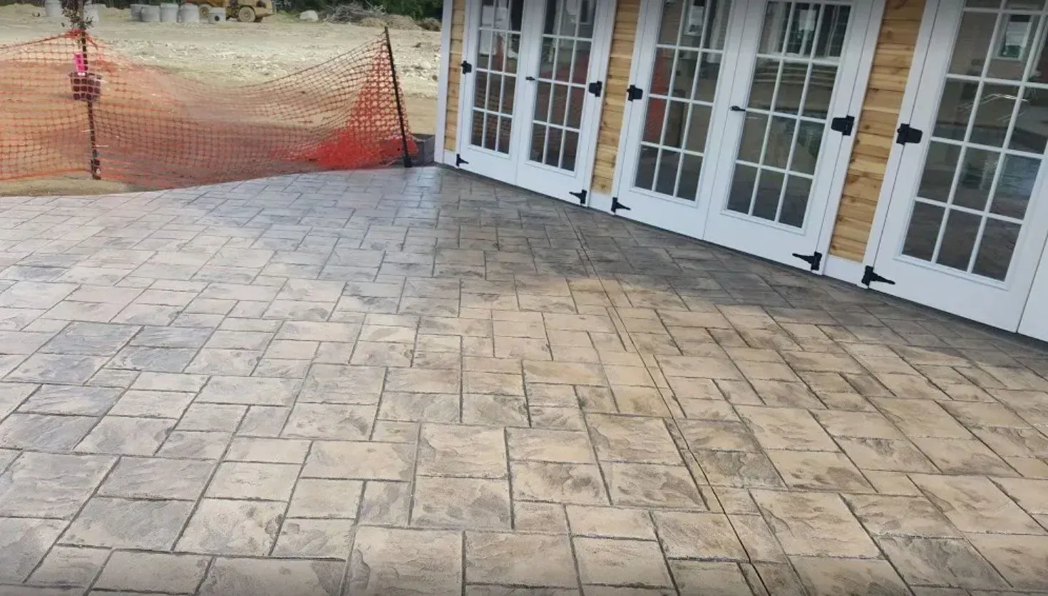 A tan stamped concrete patio with a rectangular stone pattern leads to a building with three white French doors.
