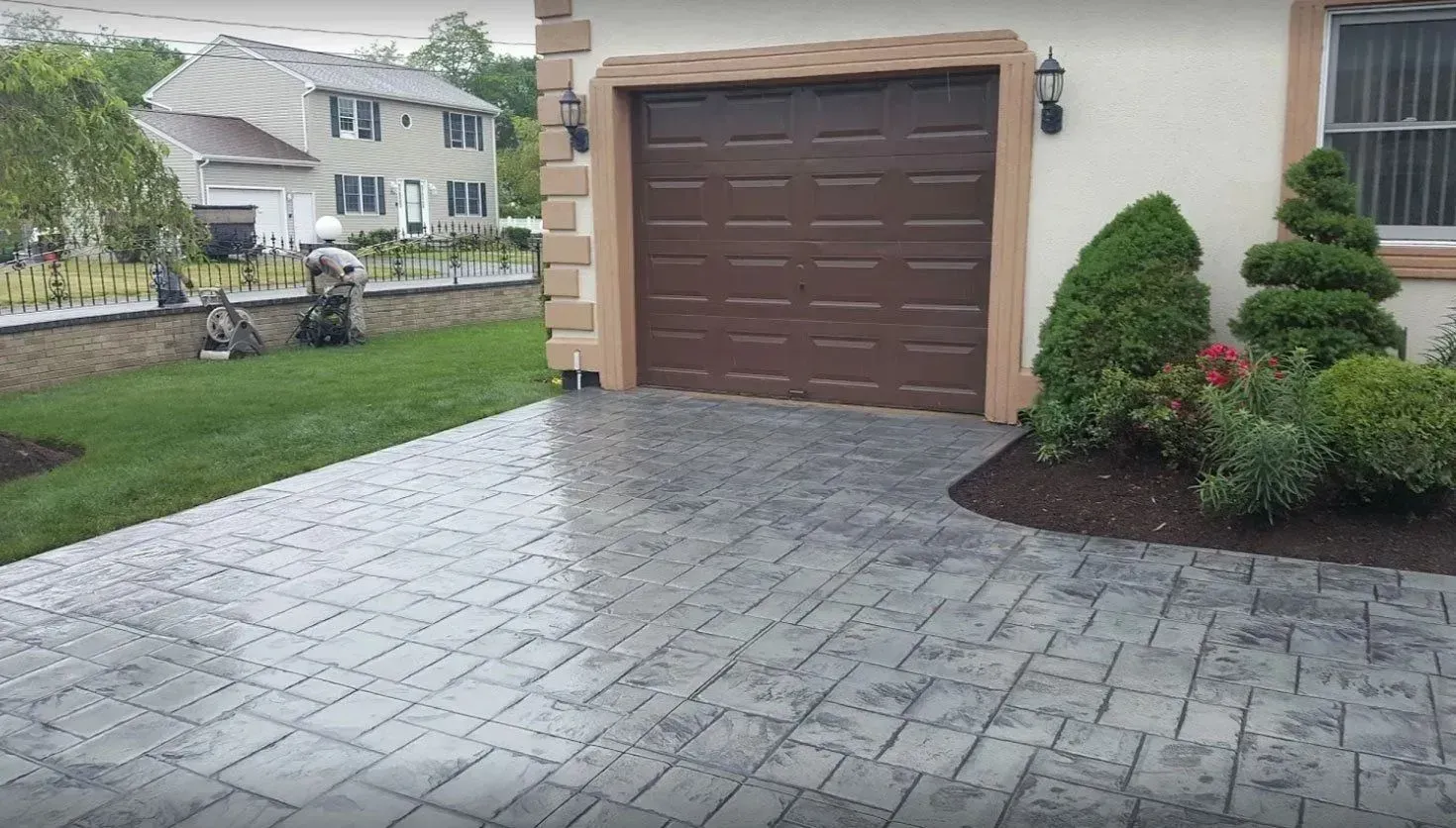 A paved driveway with a rectangular gray stone pattern leading to a residential garage with a brown door.