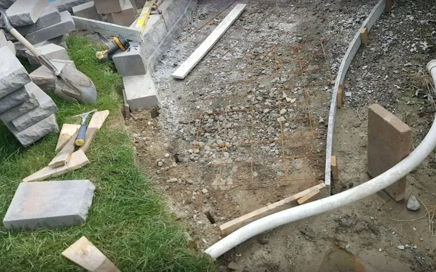 An outdoor construction site showing a curved edge formed with metal edging and wooden stakes, filled with gravel.