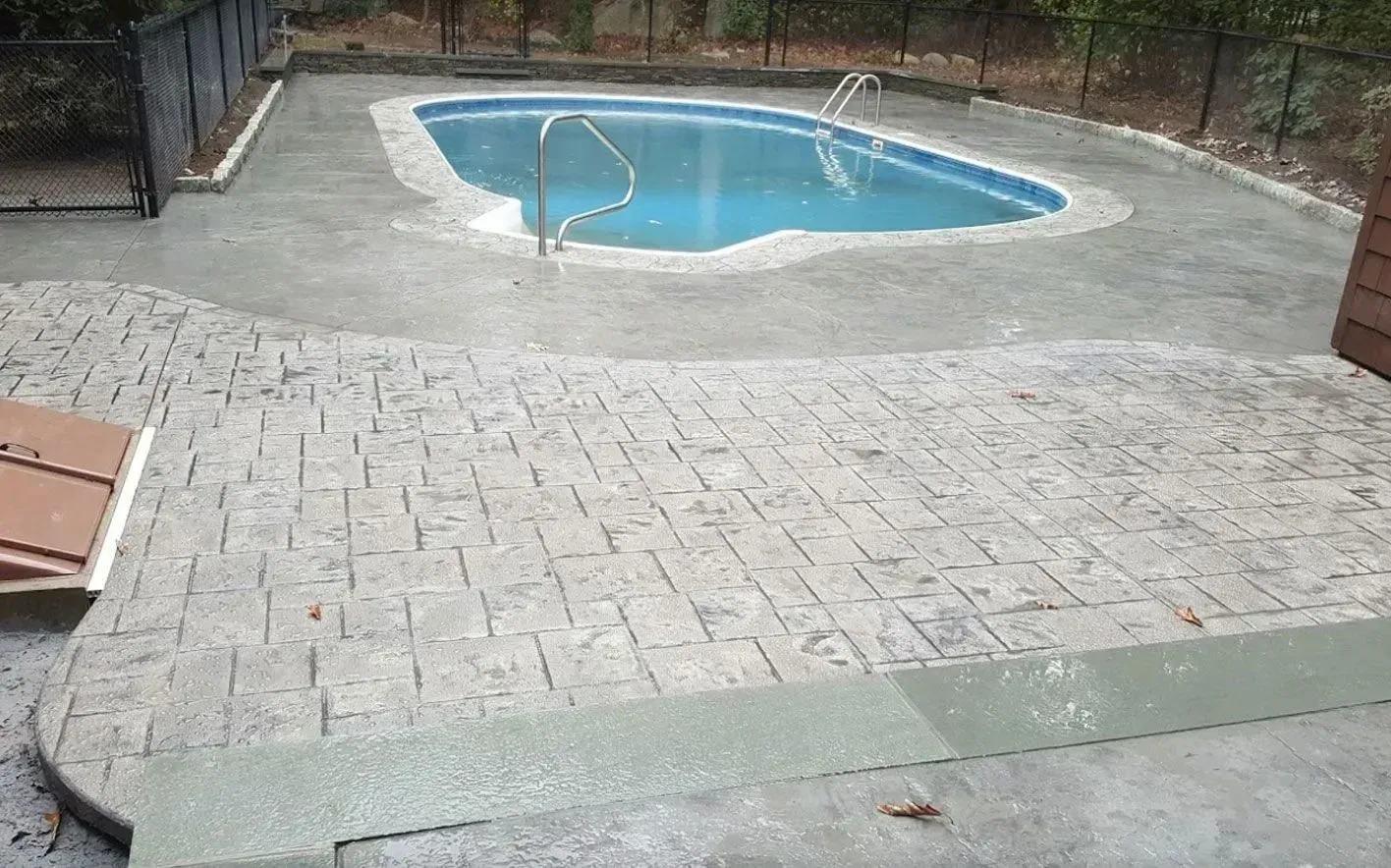 A kidney-shaped pool with a concrete deck and a stamped stone-pattern patio in a fenced backyard.