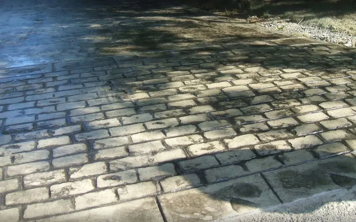 A weathered stone-paved path featuring a grid pattern, partially covered by shadows from overhead trees.