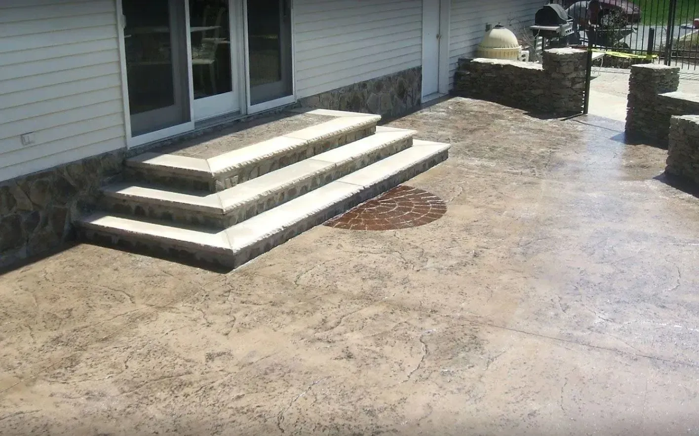 A concrete patio with a three-tier staircase leading to a house, featuring stone masonry accents on the walls and pillars.