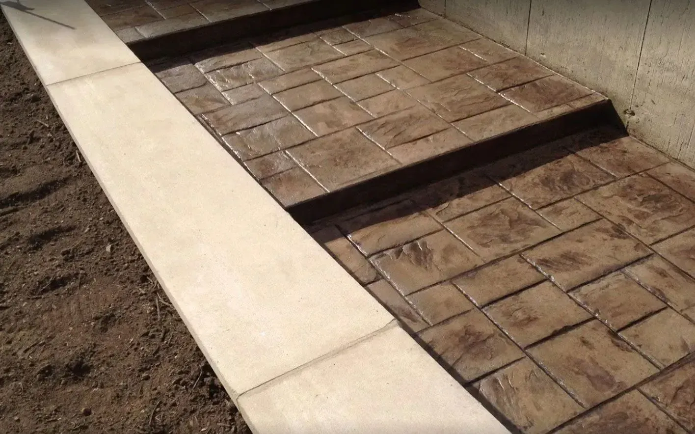 A concrete staircase featuring brown, patterned, stamped concrete treads and a smooth, light-colored concrete border.
