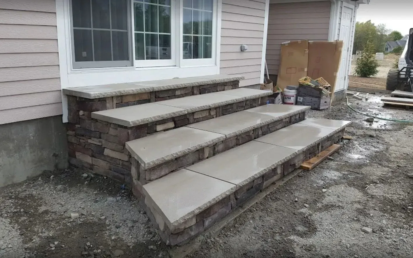 Three stone steps with concrete treads leading up to a house exterior under construction.