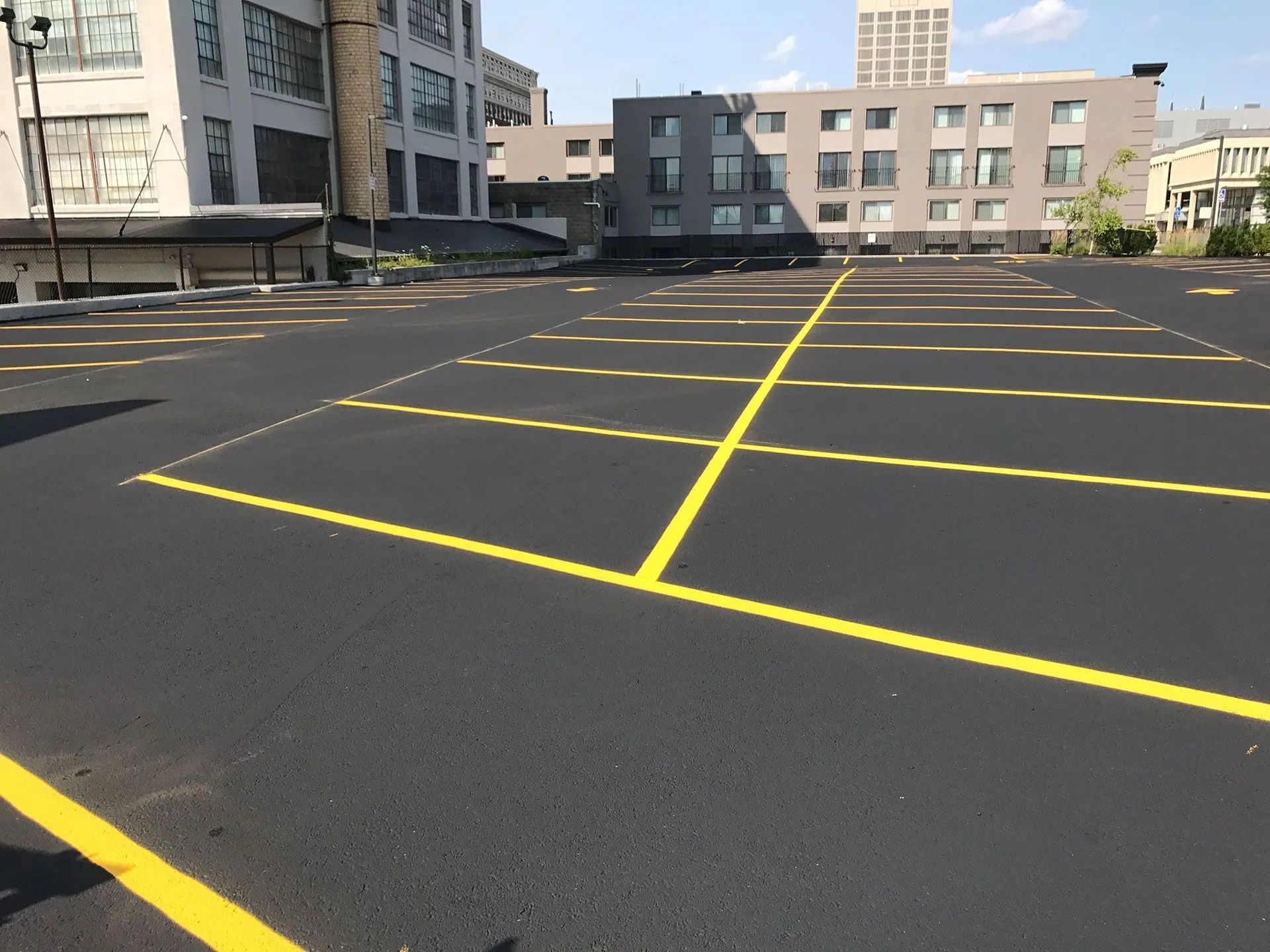 An empty asphalt parking lot with bright yellow painted lines in a city setting.