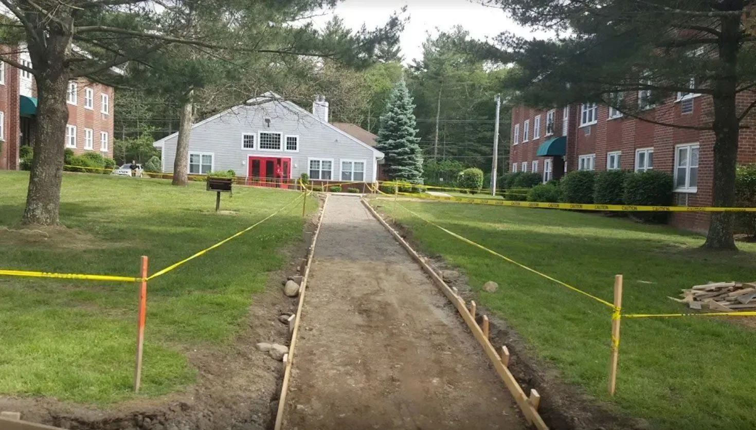 A new walkway under construction, marked by yellow caution tape, leading to a building with a light gray facade.