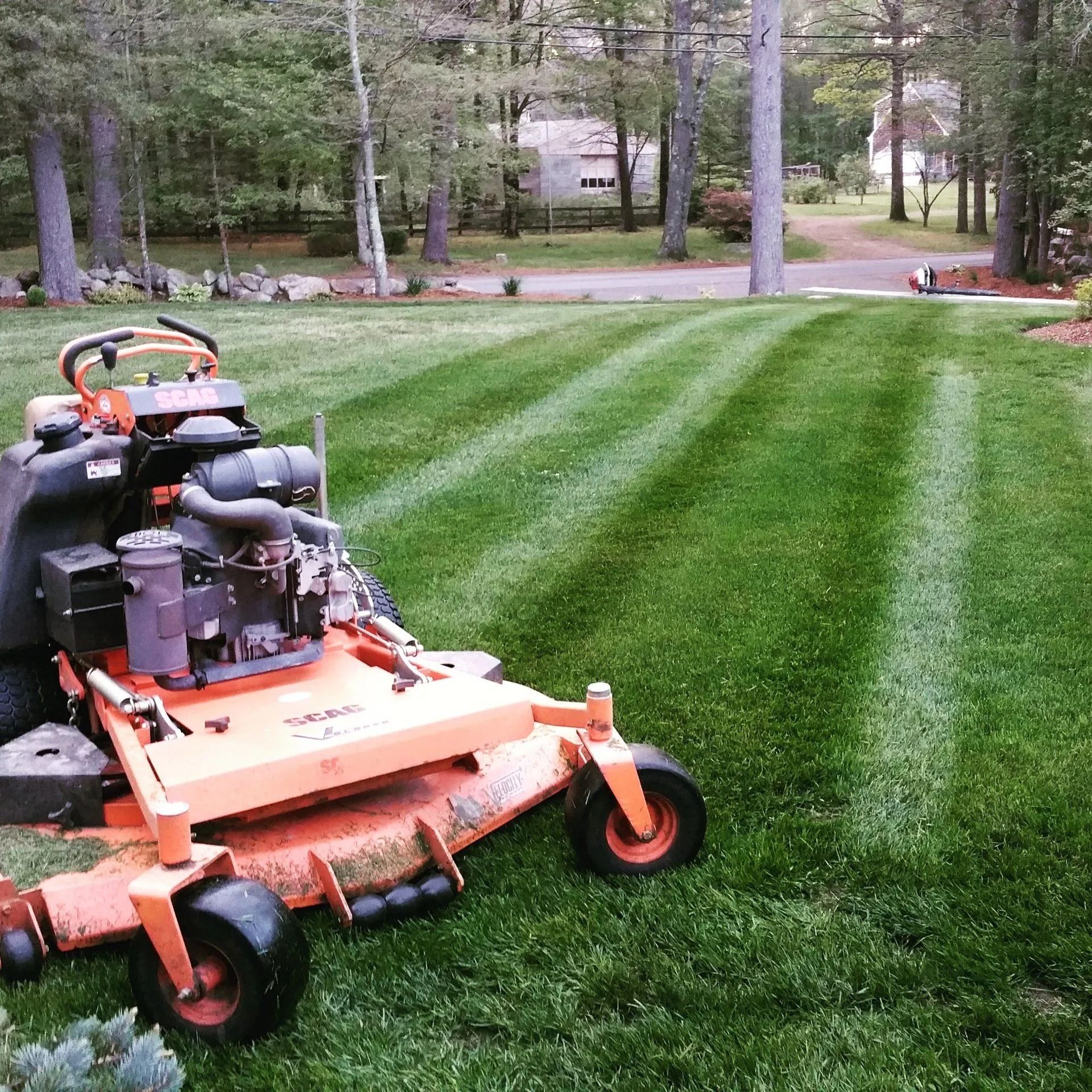 An orange commercial mower sits on a freshly cut green lawn with distinct mowing stripes in a yard with trees.