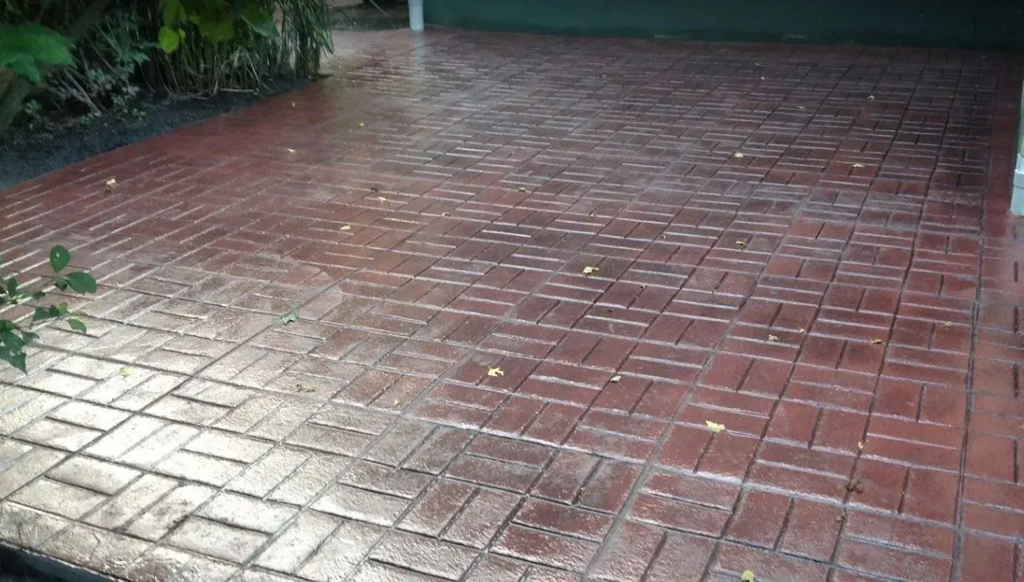 A red, herringbone-patterned paved driveway or patio surface, partially in light and partially in shadow.