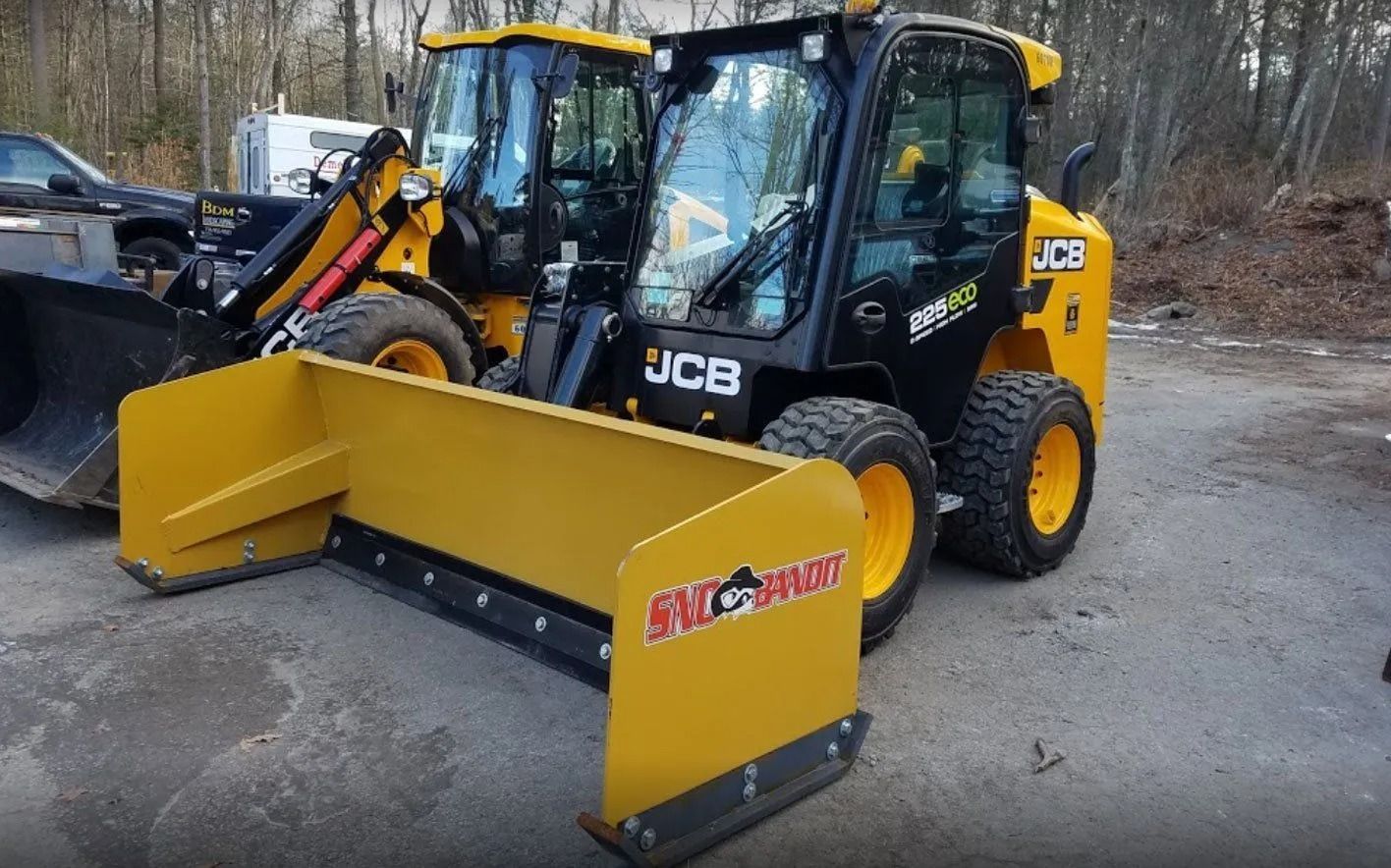 A yellow JCB skid steer loader with a large Snow Wolf snow pusher attachment parked on an asphalt lot.