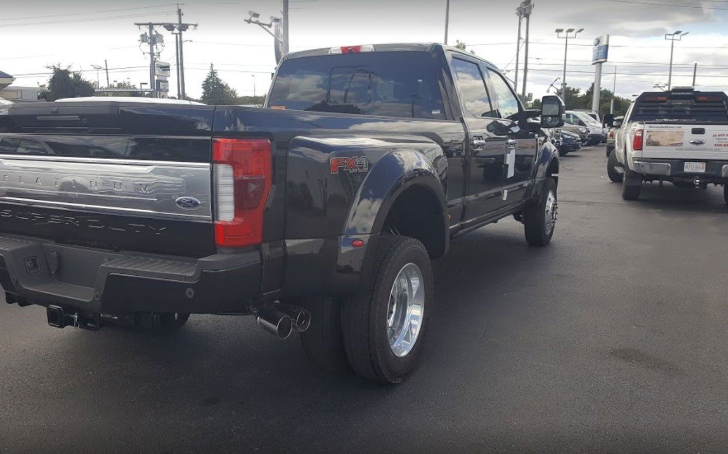 A black Ford Super Duty dual-rear-wheel pickup truck parked in a dealership lot during the day.