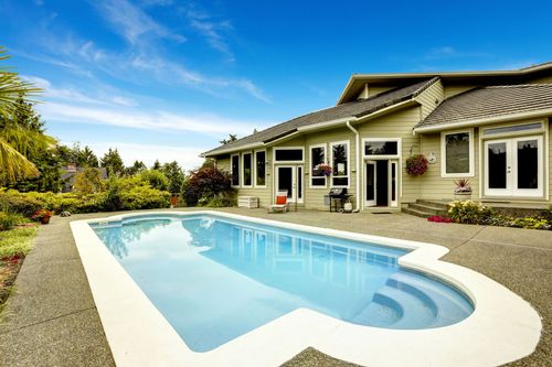 Swimming pool in front of a house with blue sky.