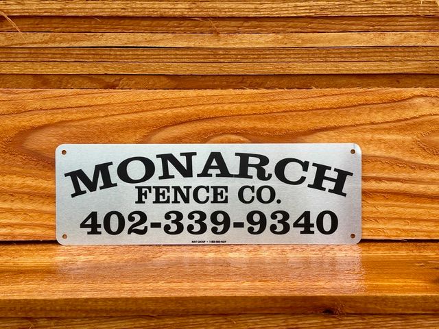 A metal Monarch Fence Co. sign with the phone number 402-339-9340 resting on wooden planks.