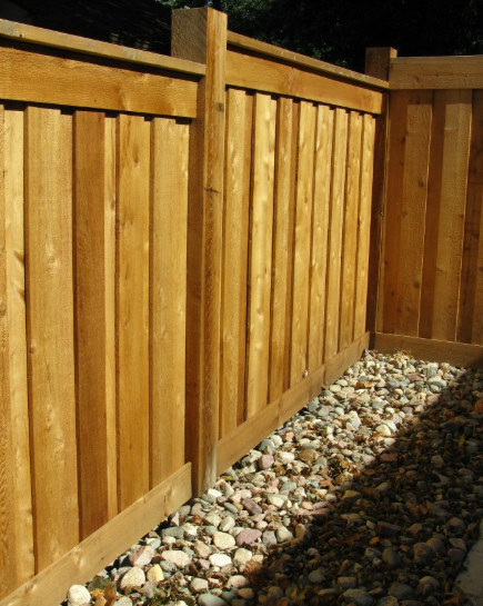A wooden privacy fence corner with vertical boards and a gravel ground cover.