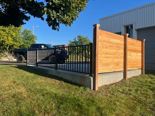 A concrete patio features a metal railing on one side and a tall, wood-slat privacy fence on the other, next to a building.