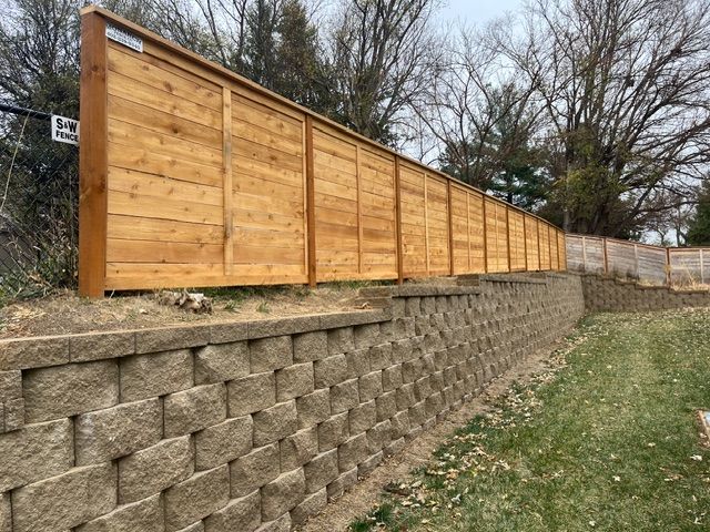 A tan concrete retaining wall topped with a horizontal wood-plank privacy fence outdoors on a cloudy day.