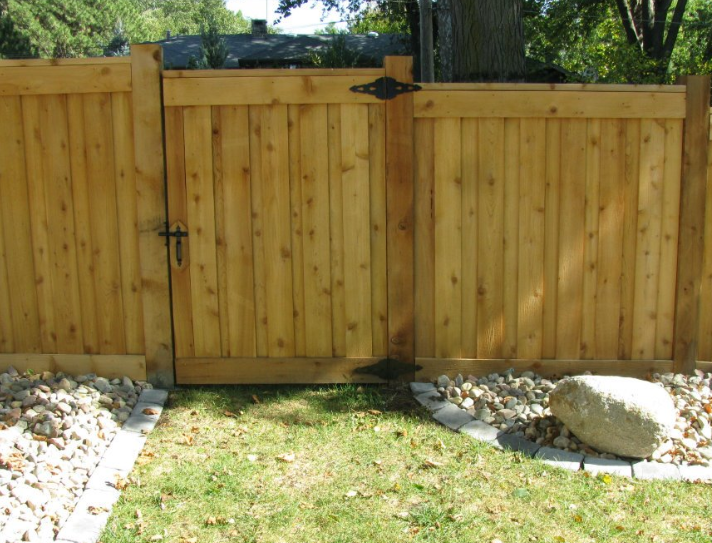 A wooden privacy fence featuring a matching gate with black hinges and latch, set above a landscaped rock border.