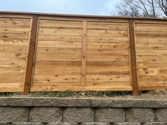 A wooden privacy fence with horizontal planks, framed by vertical posts, situated above a stacked stone retaining wall.