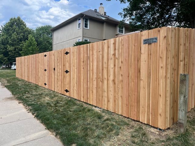 A new cedar wood privacy fence stands along a grassy sidewalk next to a suburban house.