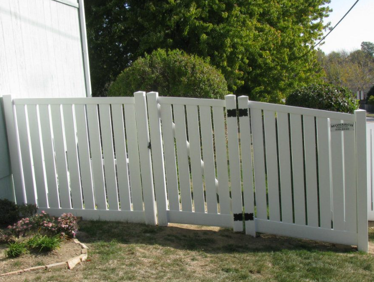 A white vinyl fence with a double gate, installed on a slight slope in a residential yard.
