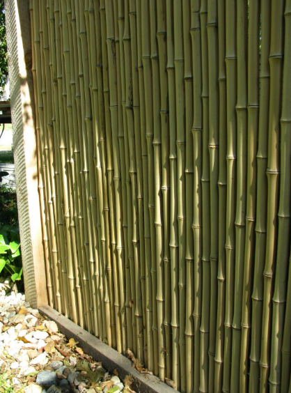 A fence made of vertical bamboo poles, framed in dark wood, set against a ground covered in light-colored pebbles.