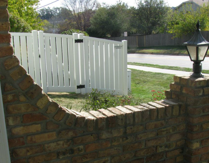 A low brick wall with a curved cutout, set in a yard with a white fence, green grass, and a black outdoor lamp post.