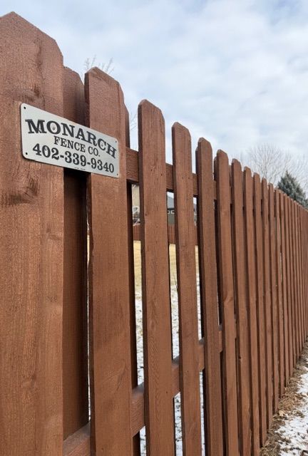 A brown wooden picket fence with a metal sign reading 