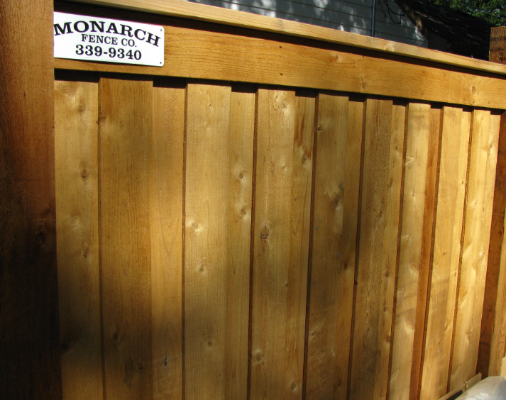 A medium-brown wood fence with a Monarch Fence Co. sign attached to the top horizontal board.