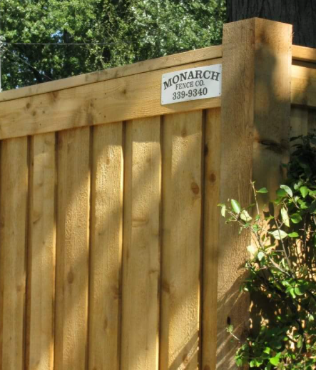 A close-up of a natural wood fence with a Monarch Fence Co. sign attached to the top rail near a wooden post.