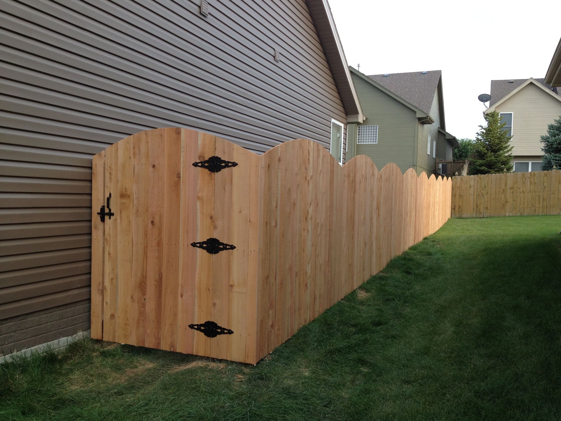 A wooden scalloped-top privacy fence attached to the side of a house, leading into a green backyard lawn.