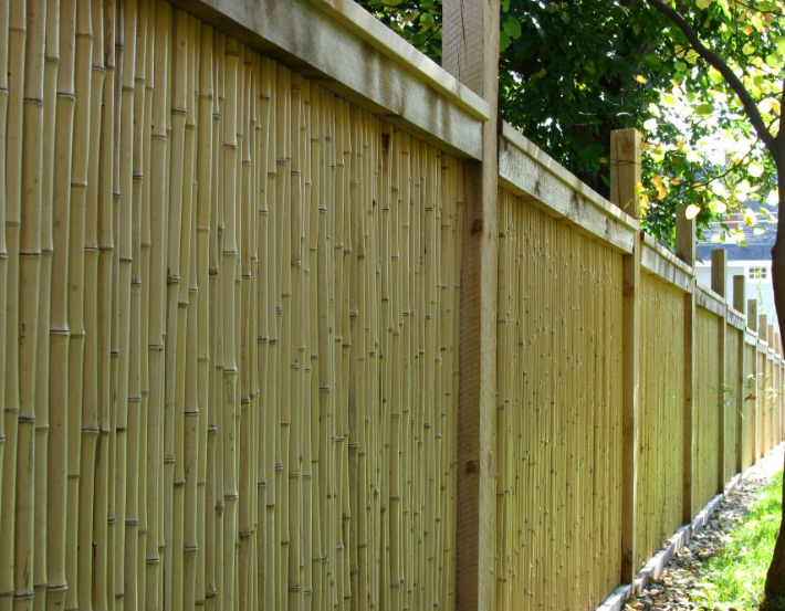 A tall fence constructed with vertical bamboo stalks, framed by horizontal wooden rails and sturdy support posts.