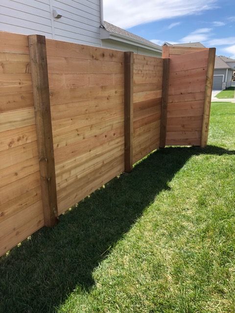 A newly installed cedar wood fence with horizontal planks and thick posts in a sunny backyard.