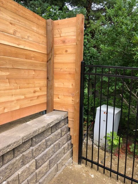 A wooden horizontal-plank fence mounted on a stone retaining wall, meeting a black metal gate at a corner.