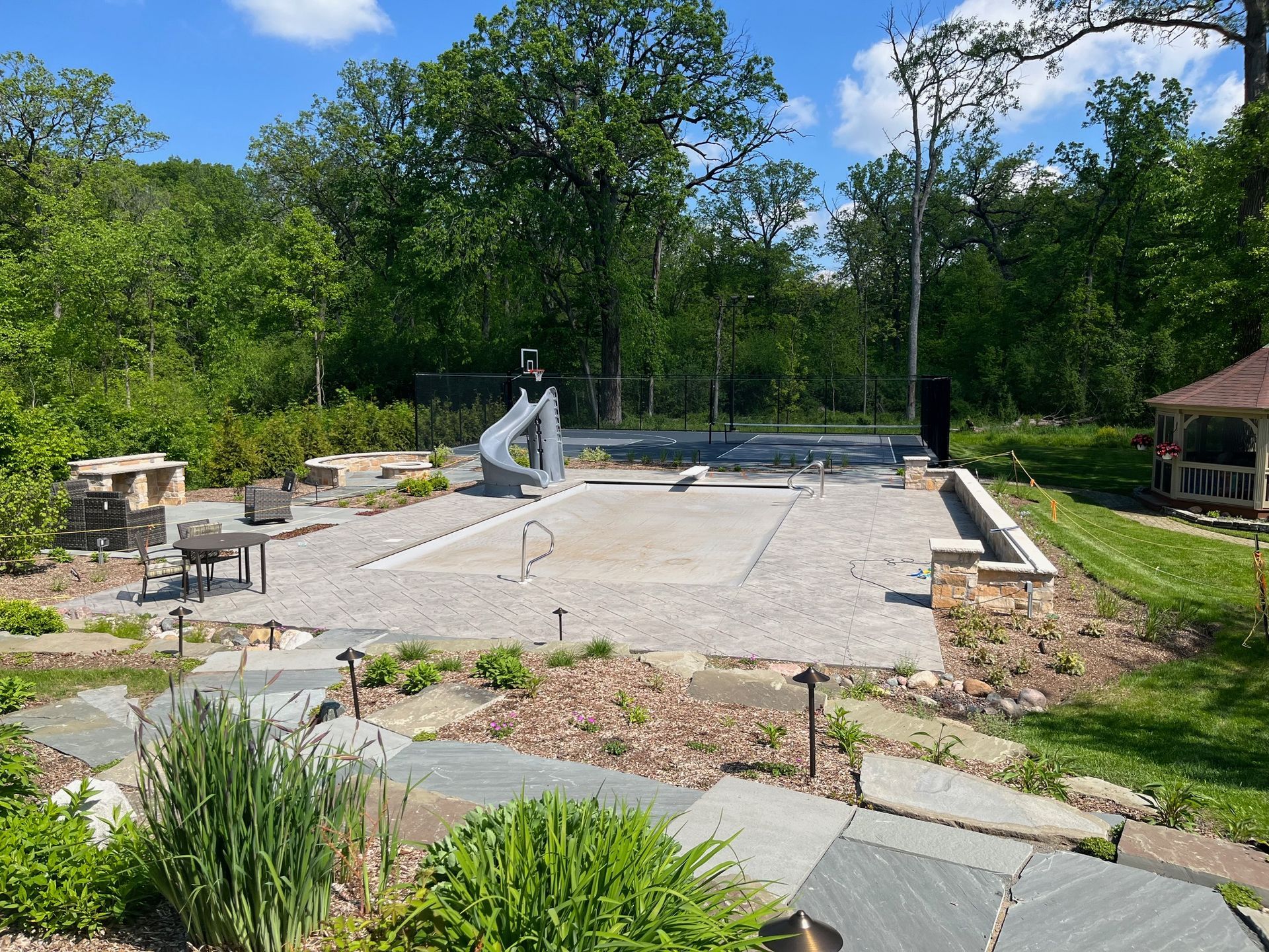 A large swimming pool is surrounded by trees and a gazebo.