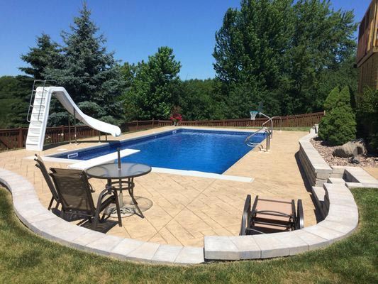 A large swimming pool with a slide and a table and chairs in the backyard.