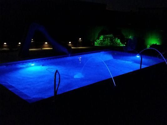A swimming pool is lit up with blue lights at night