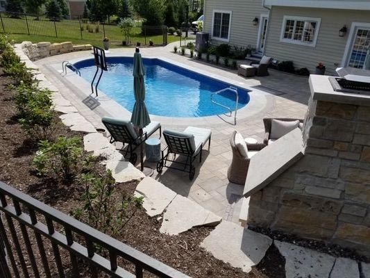A large swimming pool is surrounded by chairs and umbrellas in front of a house.