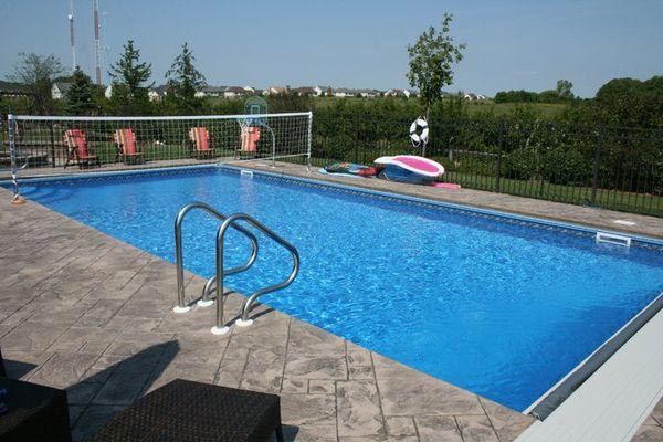 A large swimming pool is surrounded by a fence and chairs.