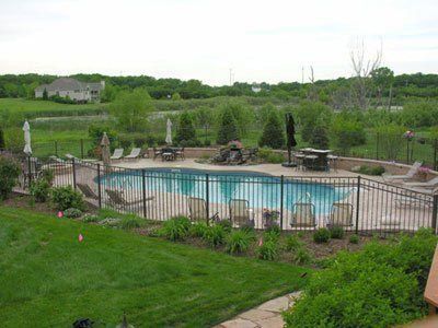 A large swimming pool surrounded by a fence and chairs in a backyard.