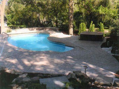 A large swimming pool is surrounded by trees and a stone patio.