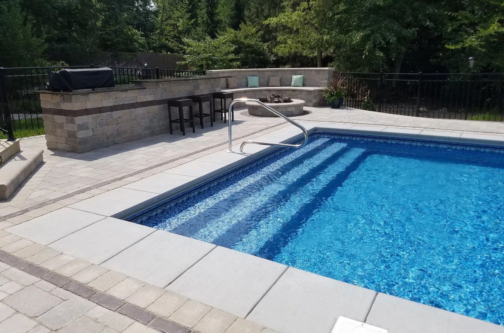 A large swimming pool with stairs and a bar in the backyard.