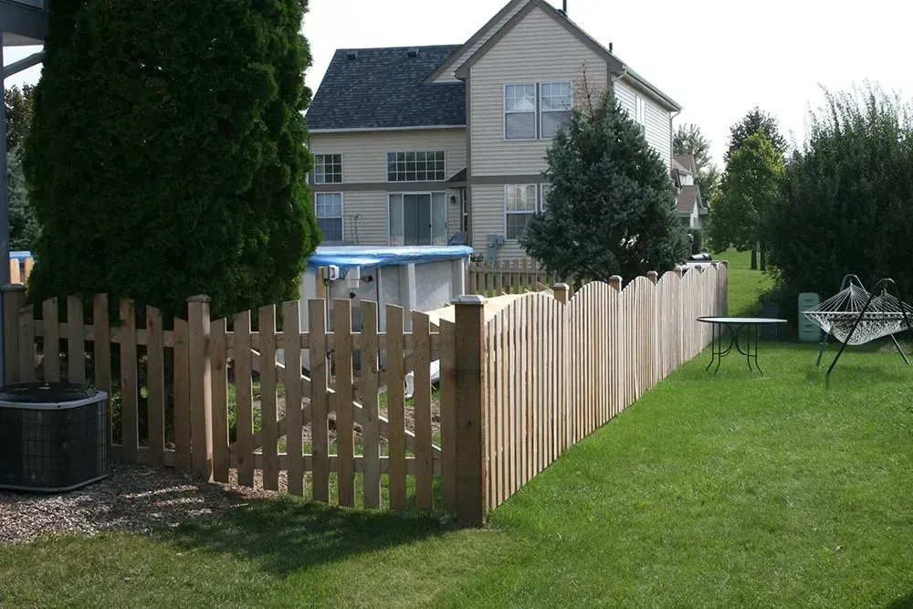 A wooden picket fence surrounds a lush green yard in front of a house