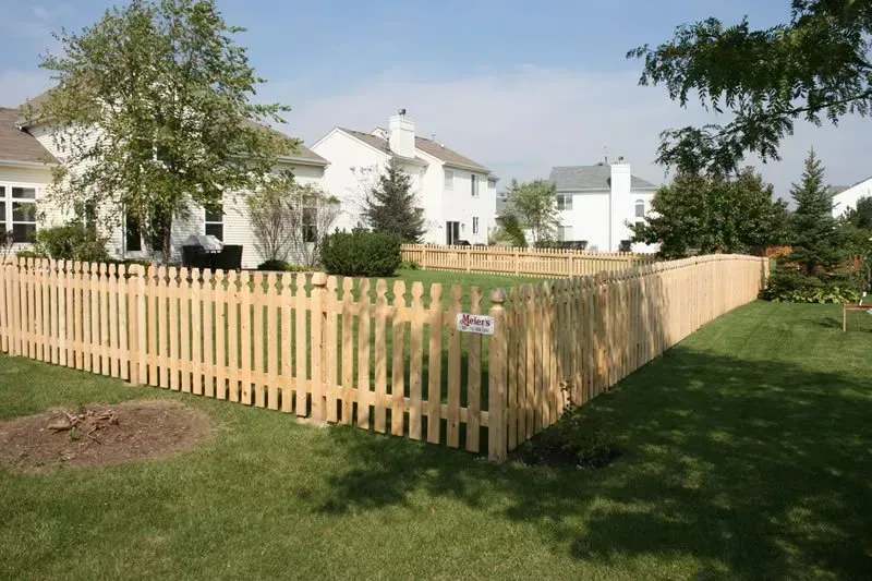 A wooden picket fence surrounds a lush green yard in front of a house.