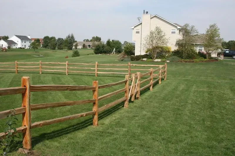 A wooden fence surrounds a lush green field in front of a house.