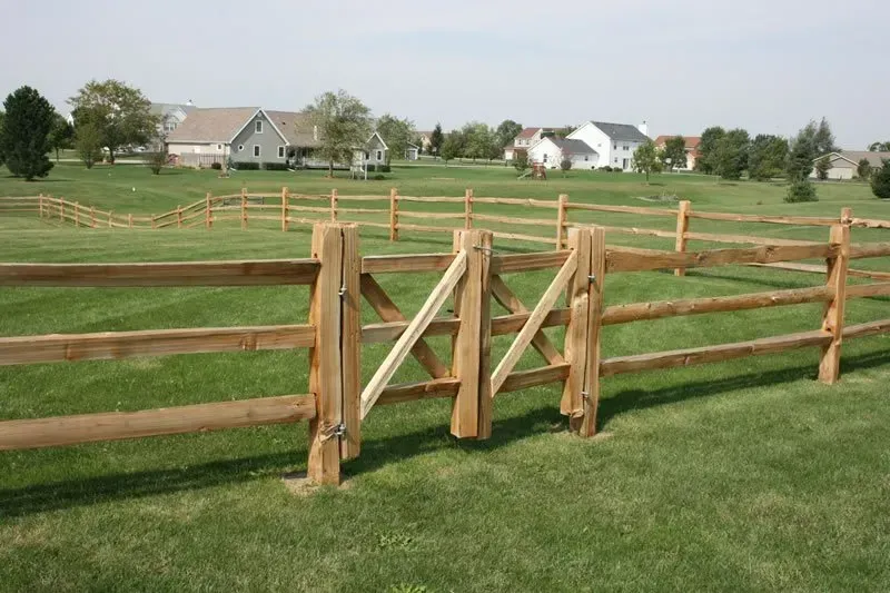 A wooden fence with a gate in the middle of a grassy field